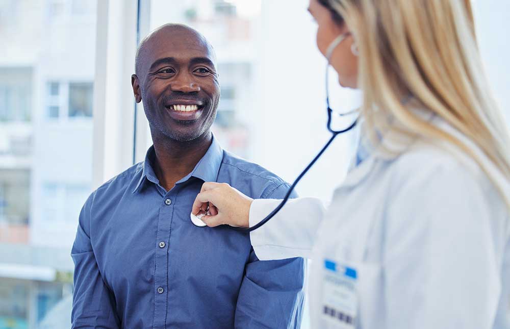 Female doctor using a stethoscope to examine a male patient during a cardiology consultation